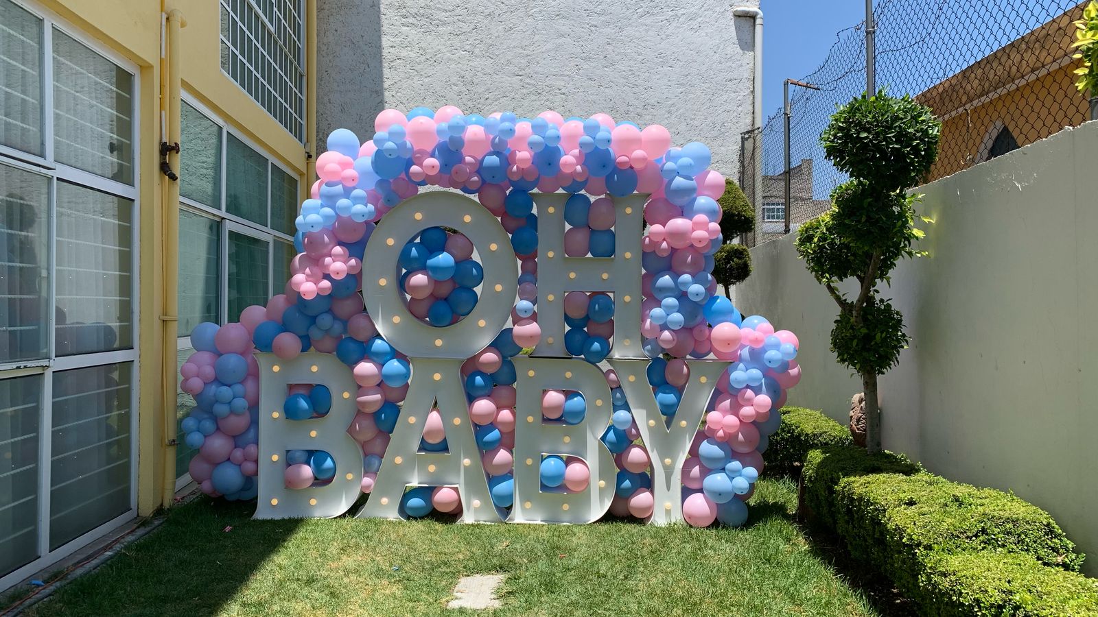 Decoracion con globos azul bebé, rosa y blanco con letrero Oh Baby y letras LED para revelación de género - Perfect Party